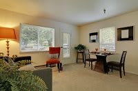 A cozy living room with a dining area, featuring a table and chairs near large windows.