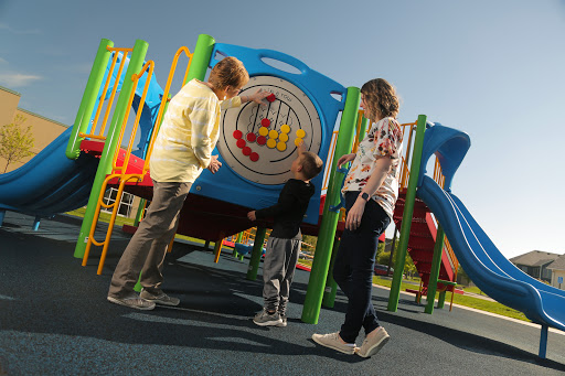A child interacts with two adults at a colorful playground, enjoying a sunny day.