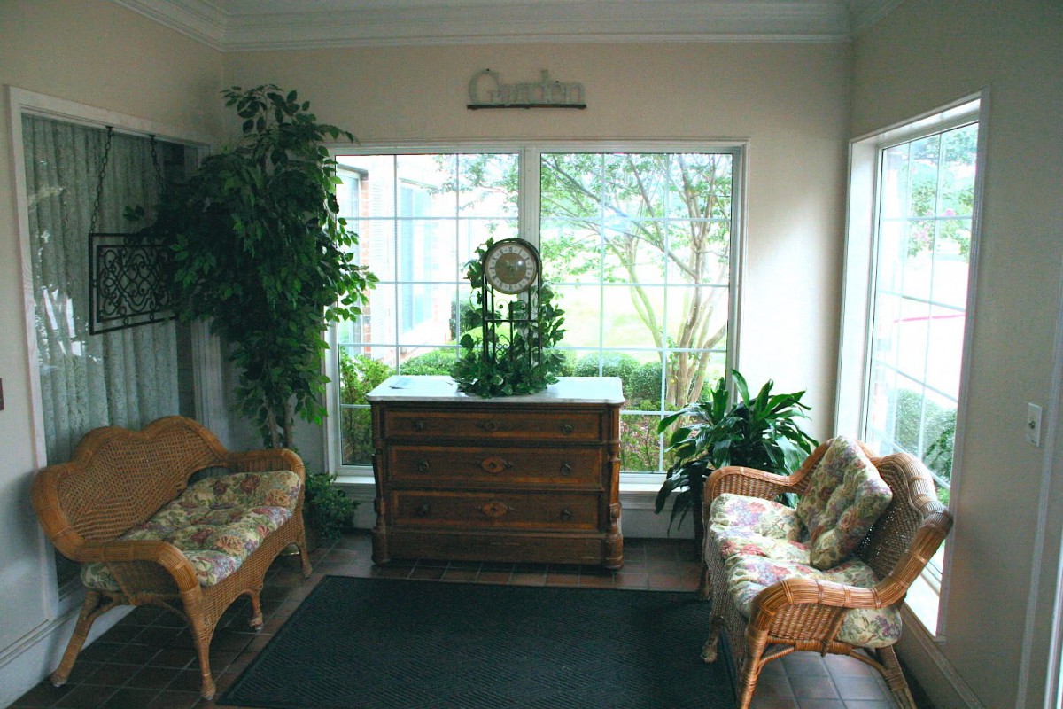 A cozy living room with wicker furniture, decorative plants, and a large window.