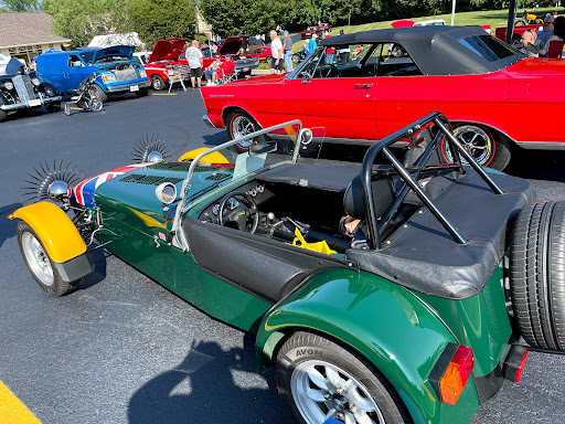 A vibrant green sports car on display at an auto show, with a variety of other vehicles in the background.