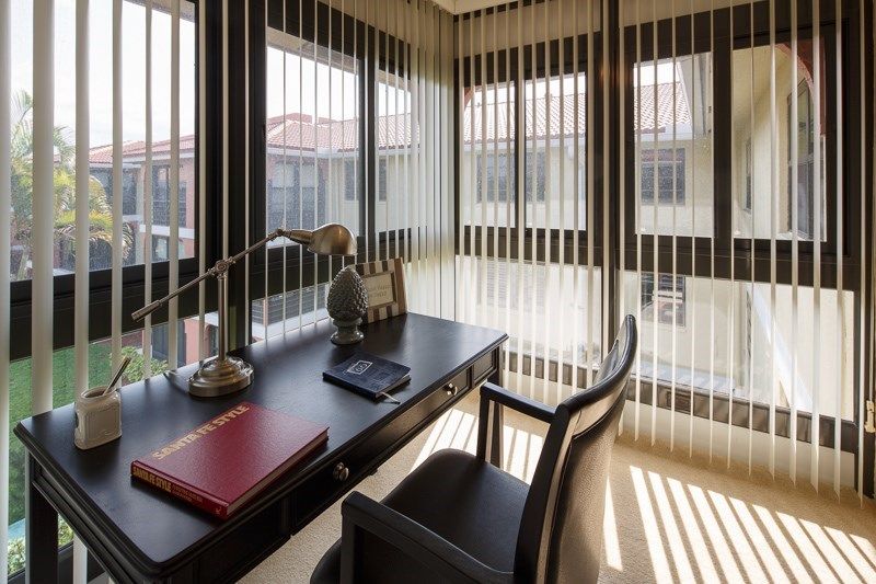 A modern office workspace featuring a desk, chair, and large windows with blinds.