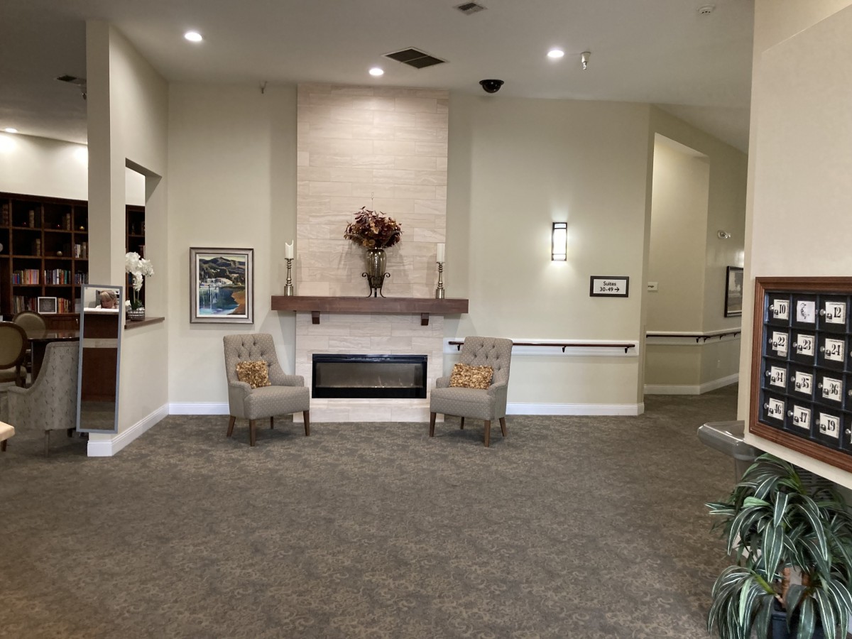 A cozy lobby area featuring a fireplace with two chairs and subtle decor.