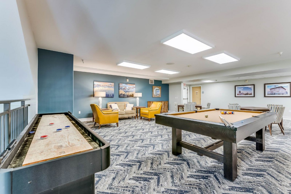 A modern game room featuring a shuffleboard, pool table, and comfortable seating area.