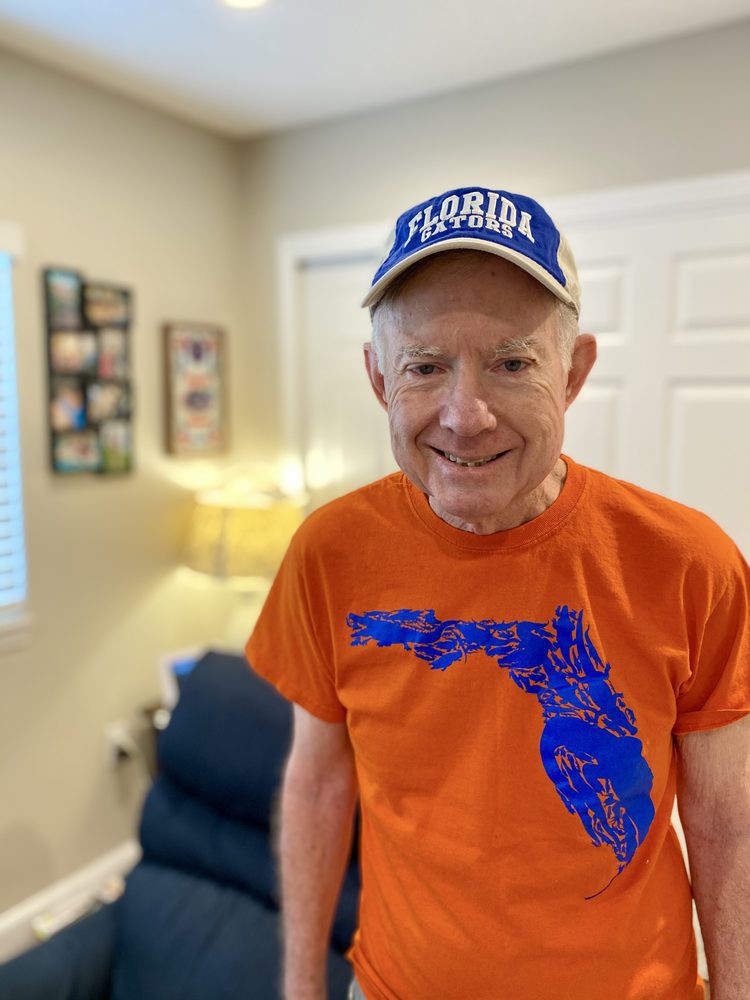 A man wearing a Florida T-shirt and cap stands in a room.