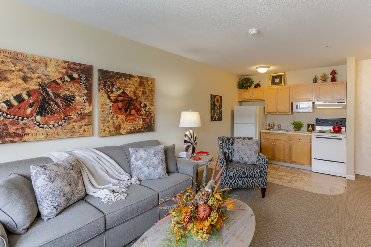 A cozy living space with comfortable seating, artwork on the walls, and a kitchenette in the background.