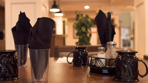 A cozy restaurant table set with black napkins, cups, and condiments, offering a welcoming atmosphere.