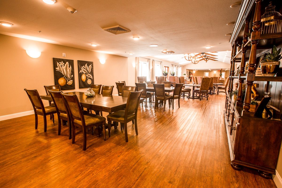 A spacious dining area with wooden flooring, furnished with tables and chairs.