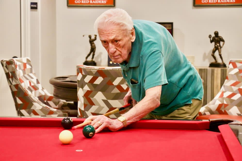 An elderly person playing billiards on a red pool table.