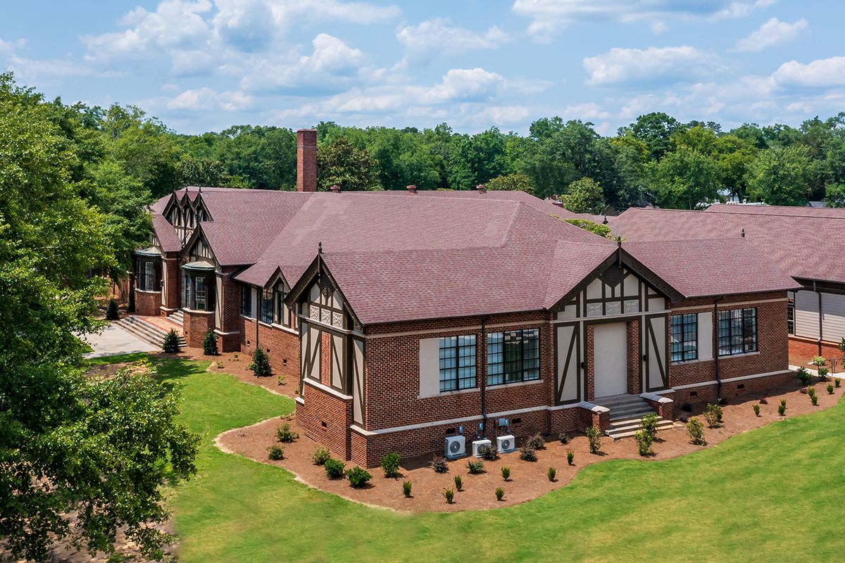 A large brick building with a traditional architectural style surrounded by lush greenery.