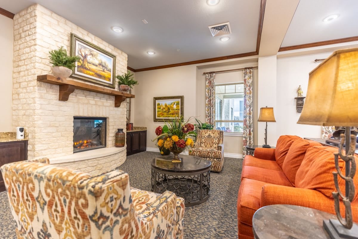 A cozy living room with a sofa, armchairs, and a fireplace, featuring elegant decor and paintings.