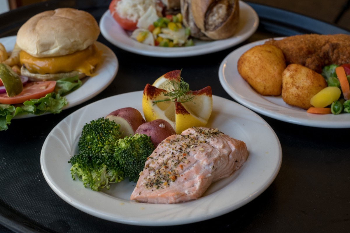 A meal featuring seasoned salmon, broccoli, and potatoes on a plate, with other dishes in the background.