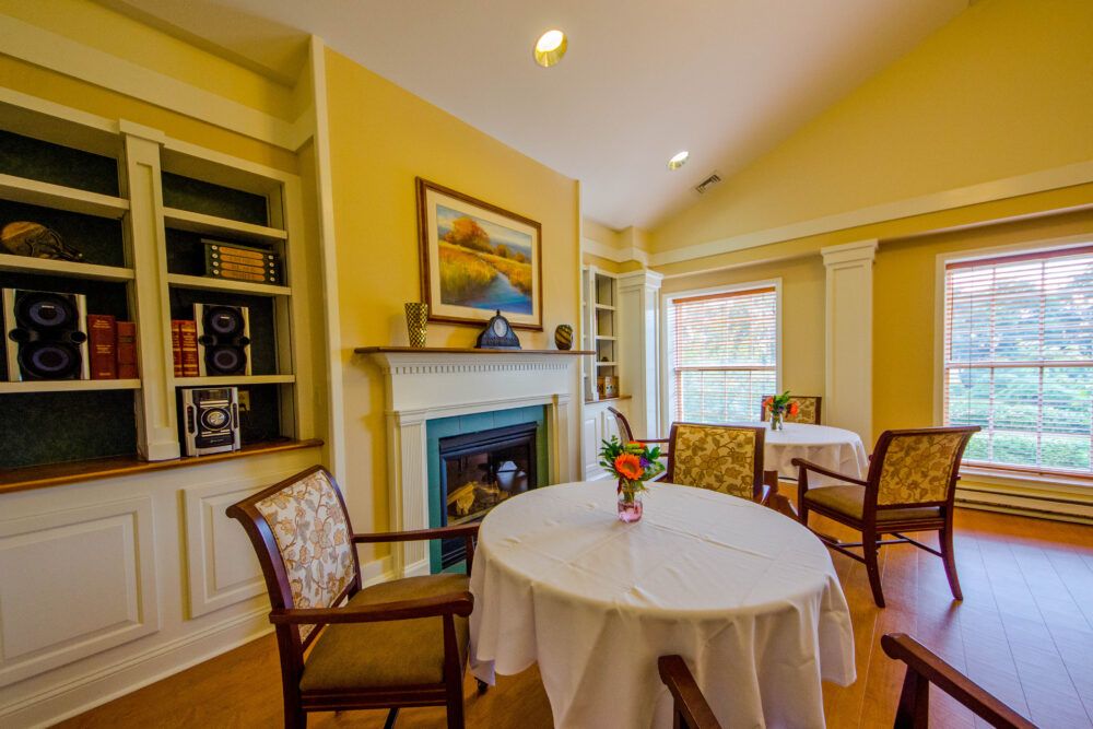 A cozy dining area with a table and chairs, featuring a fireplace and decorative shelves.