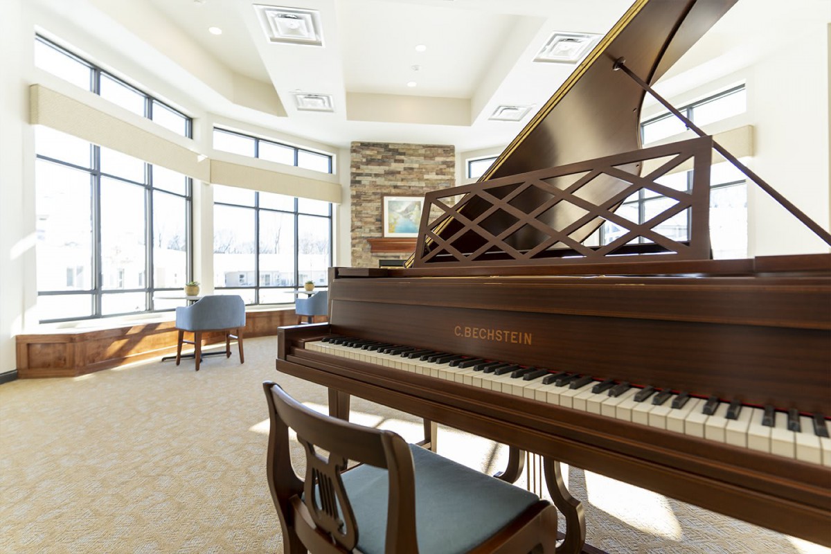 A spacious music room featuring a grand piano, with abundant natural light streaming through large windows.