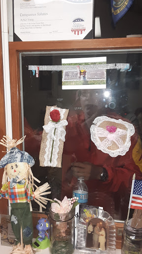 A window display featuring handmade crafts, including lace decorations and a straw figure.