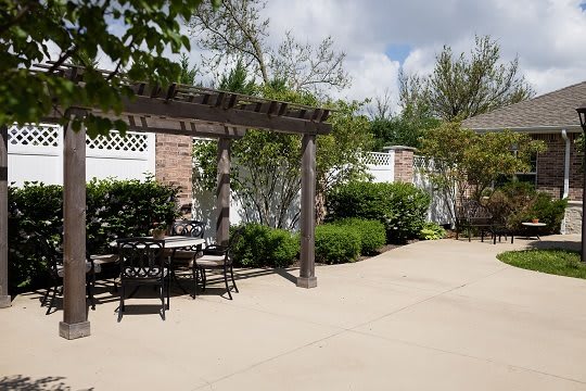 A sunny patio area featuring a pergola with outdoor furniture and lush garden surroundings.