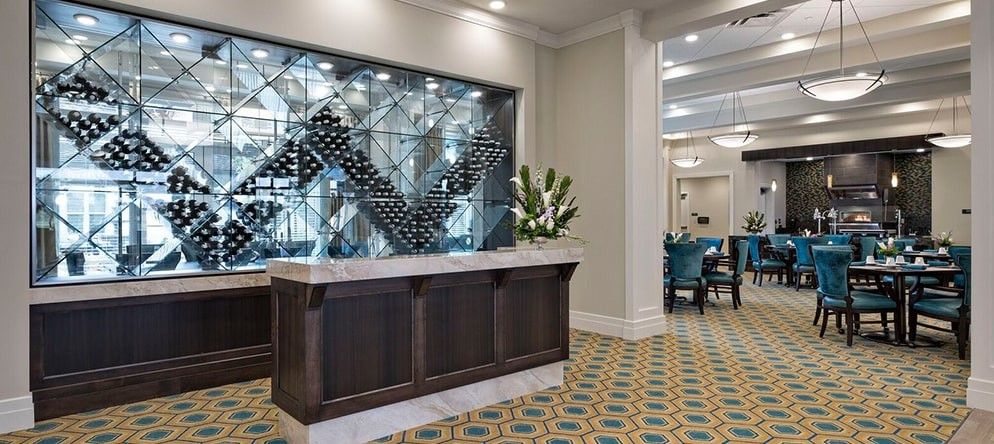 A modern and elegant hotel lobby featuring a reception desk with a decorative wine rack and floral arrangement.