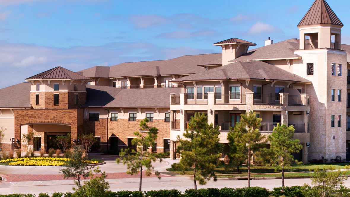 Exterior view of a modern residential apartment complex with greenery and a clear sky.