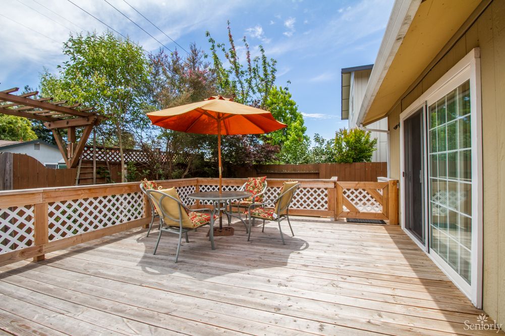 A sunny outdoor patio with a table and chairs, featuring an orange umbrella.