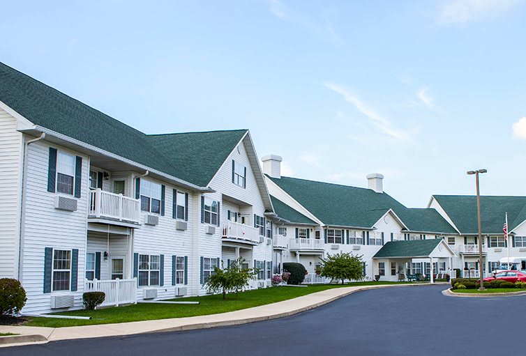 A modern residential housing complex with green roofs and white exteriors, featuring multiple balconies along a paved driveway.