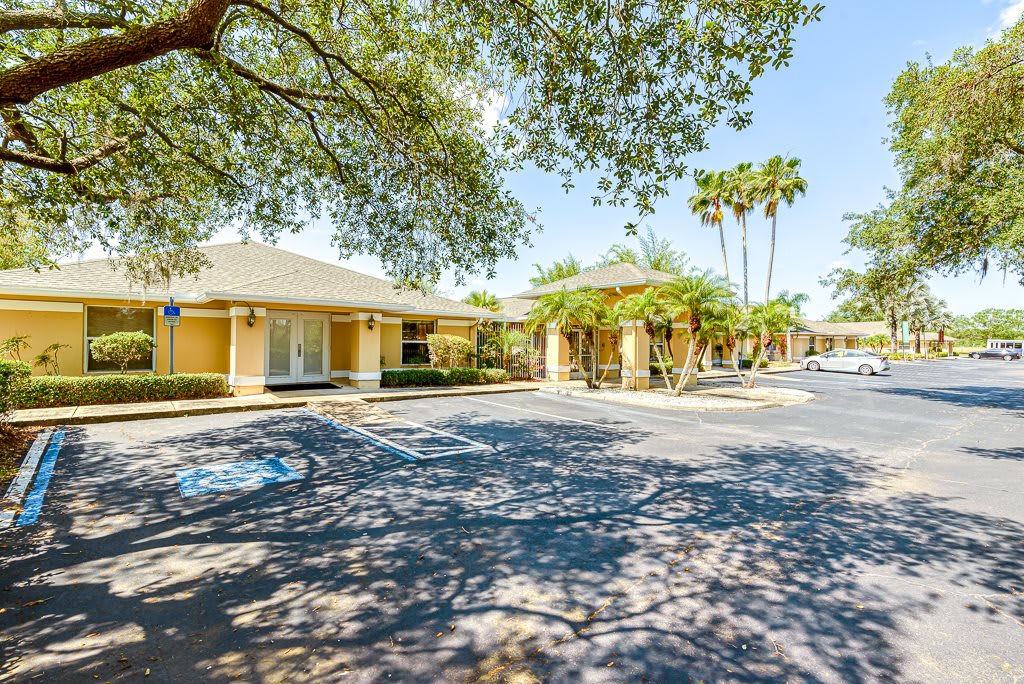 A sunny day view of a motel with a parking lot and surrounding trees.