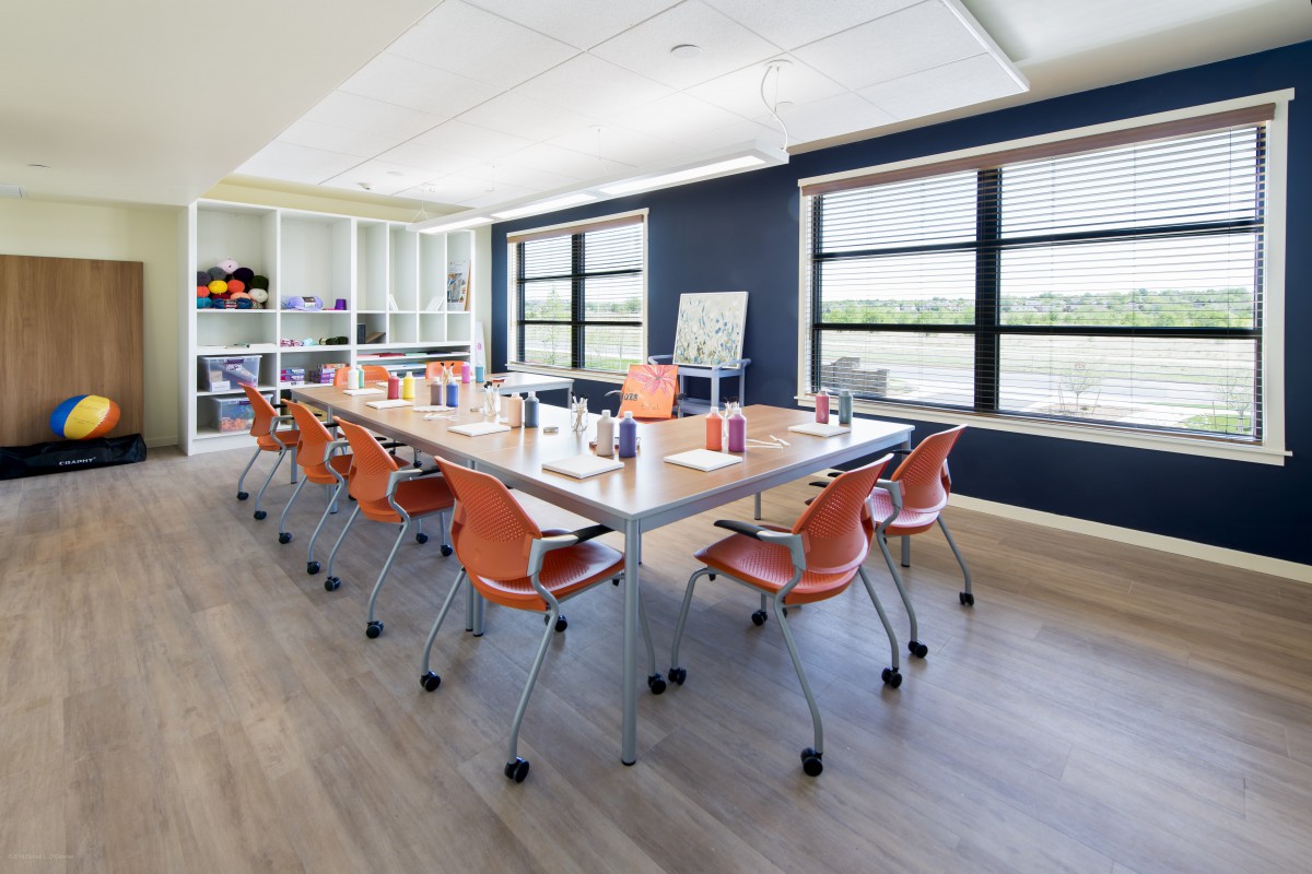 A modern meeting room with a large conference table and orange chairs, illuminated by natural light from wide windows.
