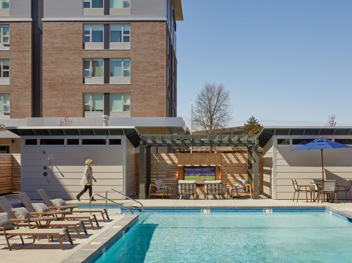An outdoor swimming pool area with sunbeds and a view of an adjacent building on a clear day.