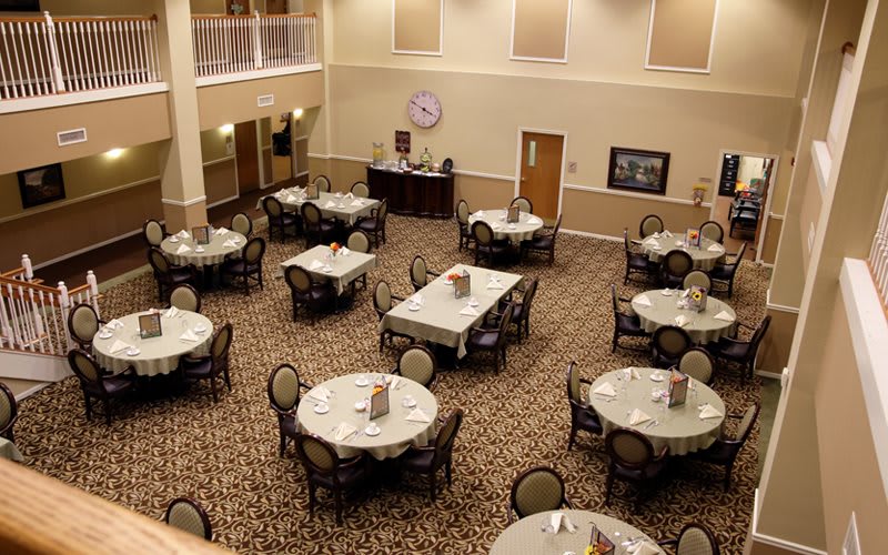 An empty dining hall with round tables and chairs arranged neatly on a carpeted floor.