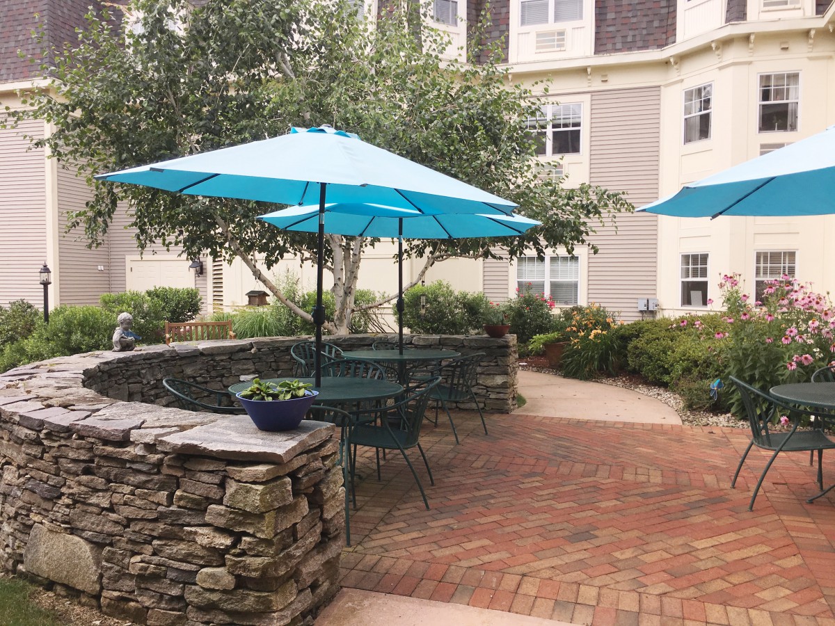 A cozy outdoor patio area with turquoise umbrellas and a stone wall surrounded by greenery.