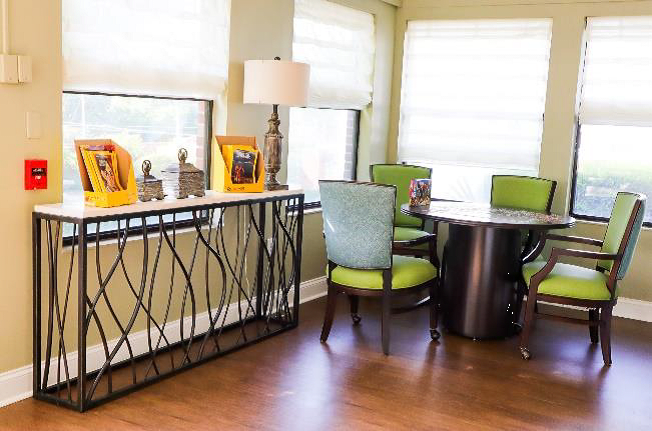 A cozy living room corner with a round table and vibrant green chairs, accented by decorative pieces on a console table.