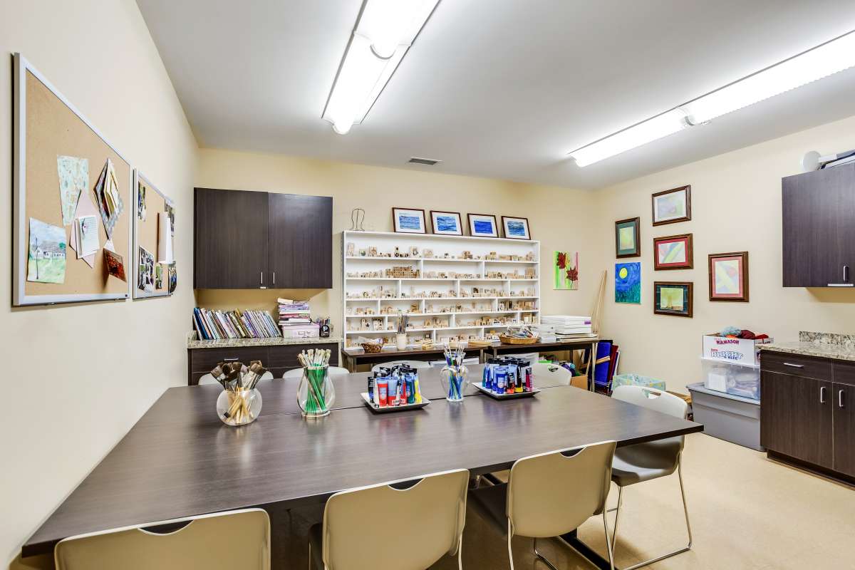 A well-organized art studio with tables, chairs, and shelves filled with art supplies.