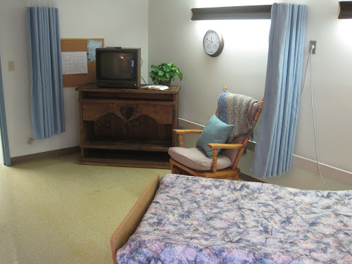 A cozy room featuring a bed, television, and rocking chair with soft blue curtains.