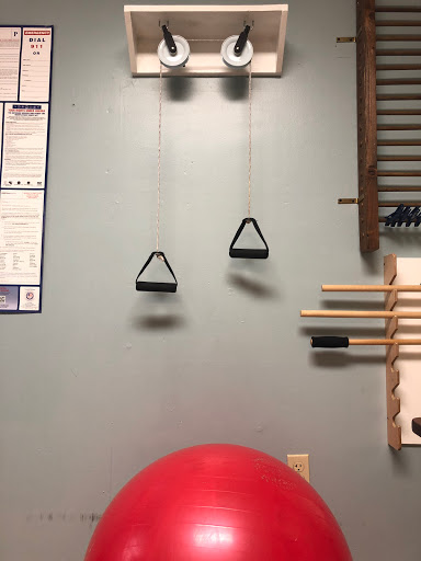 A wall-mounted exercise setup featuring pulleys and a stability ball.