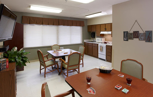 A cozy kitchen and dining area with a wooden table and chairs, featuring white appliances and blinds on the windows.