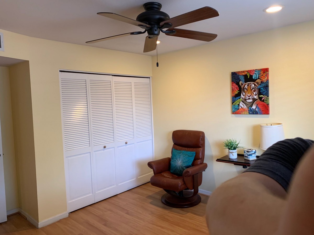 A cozy room featuring a brown chair, a colorful painting, and a ceiling fan.
