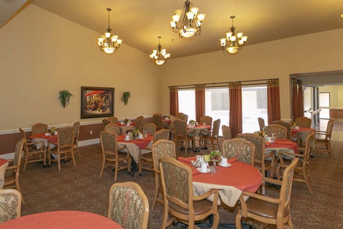A well-lit dining room featuring several tables and chairs, illuminated by chandeliers.