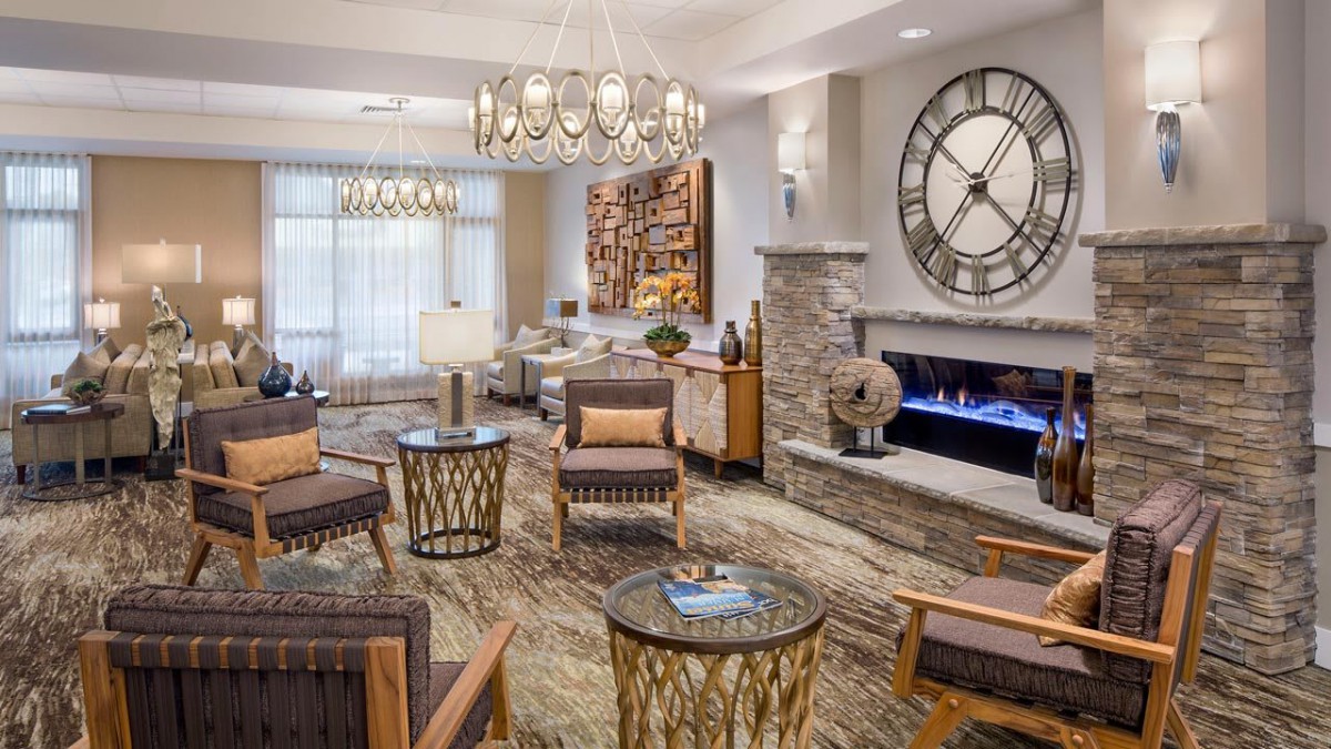 A modern living room with a large wall clock, fireplace, and stylish seating arrangement.