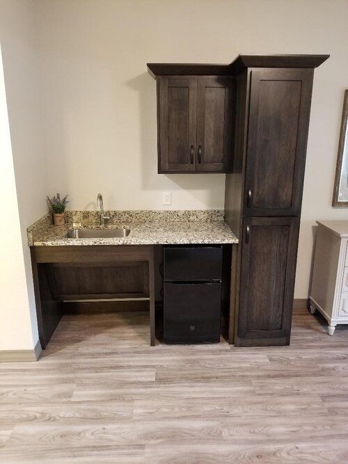 A modern kitchenette with dark wood cabinets, granite countertop, and a small sink.
