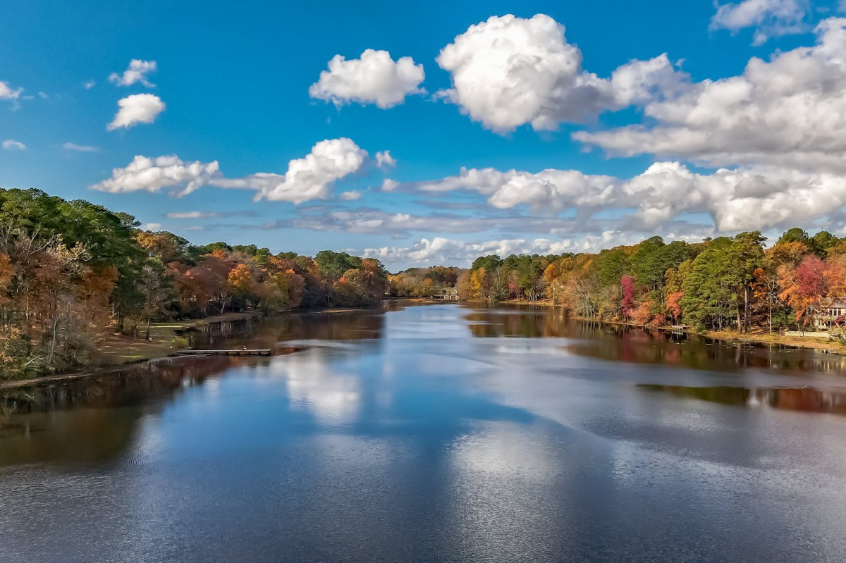 A serene autumn landscape with a river reflecting the cloudy sky and surrounded by colorful trees.