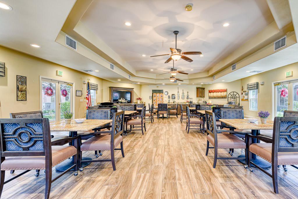 A spacious dining area with neatly arranged tables and chairs, featuring ceiling fans and warm lighting.