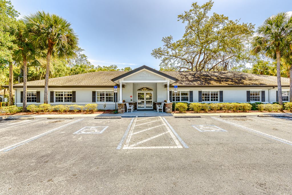 A single-story house with a parking area in front, surrounded by trees and clear blue skies.