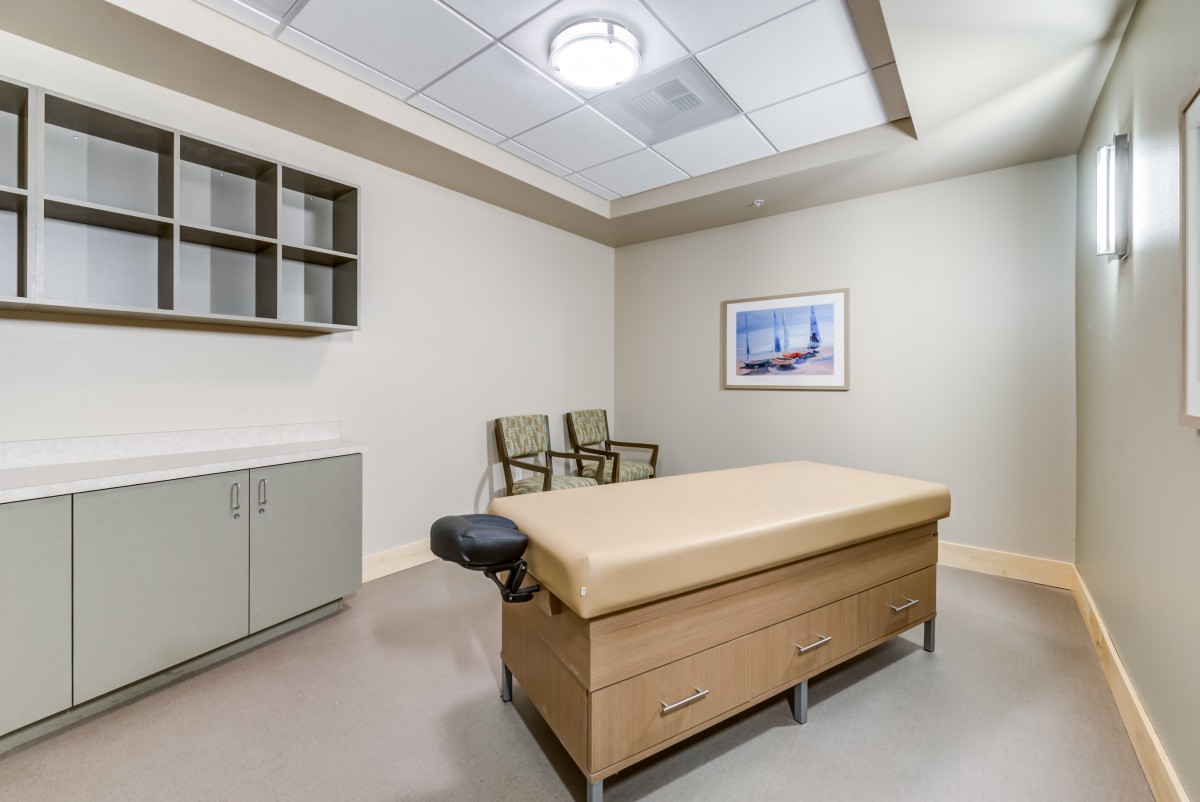 A modern medical examination room with a treatment table and seating.