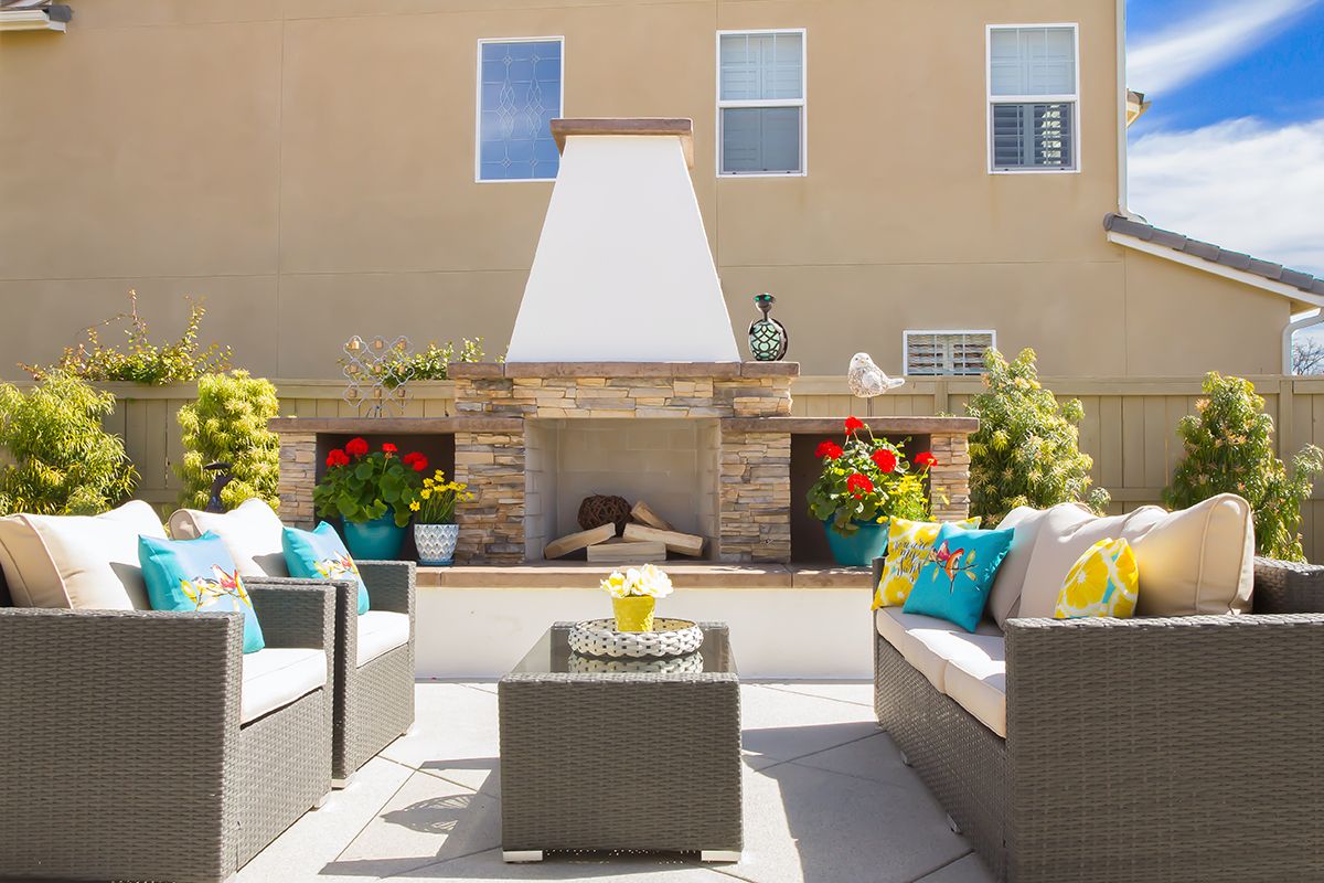 A beautifully decorated outdoor patio with a central fireplace and comfortable seating.