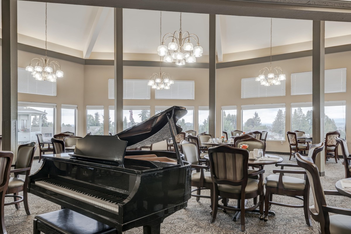 An elegant dining room featuring a grand piano and large windows.