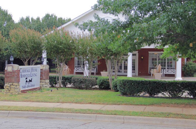 A large red-brick building with white columns and a neatly landscaped front yard.