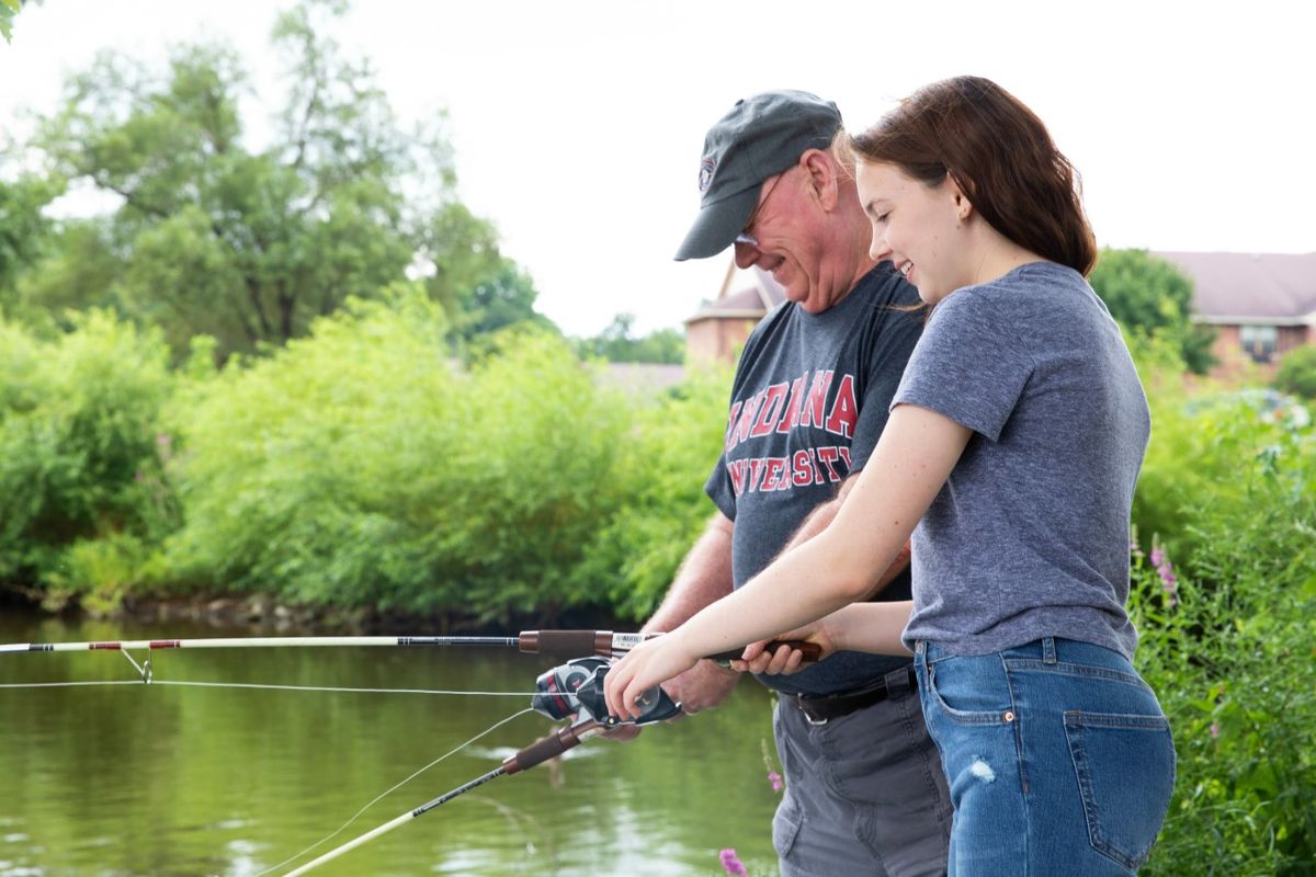 A pair of people enjoy fishing together by a lake, surrounded by nature.