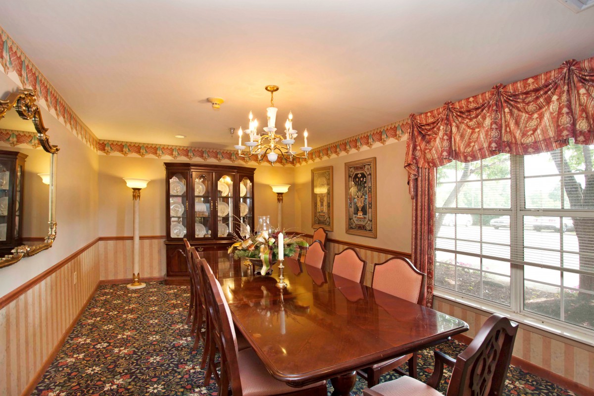 An elegant dining room featuring a long wooden table, a chandelier, and a china cabinet.