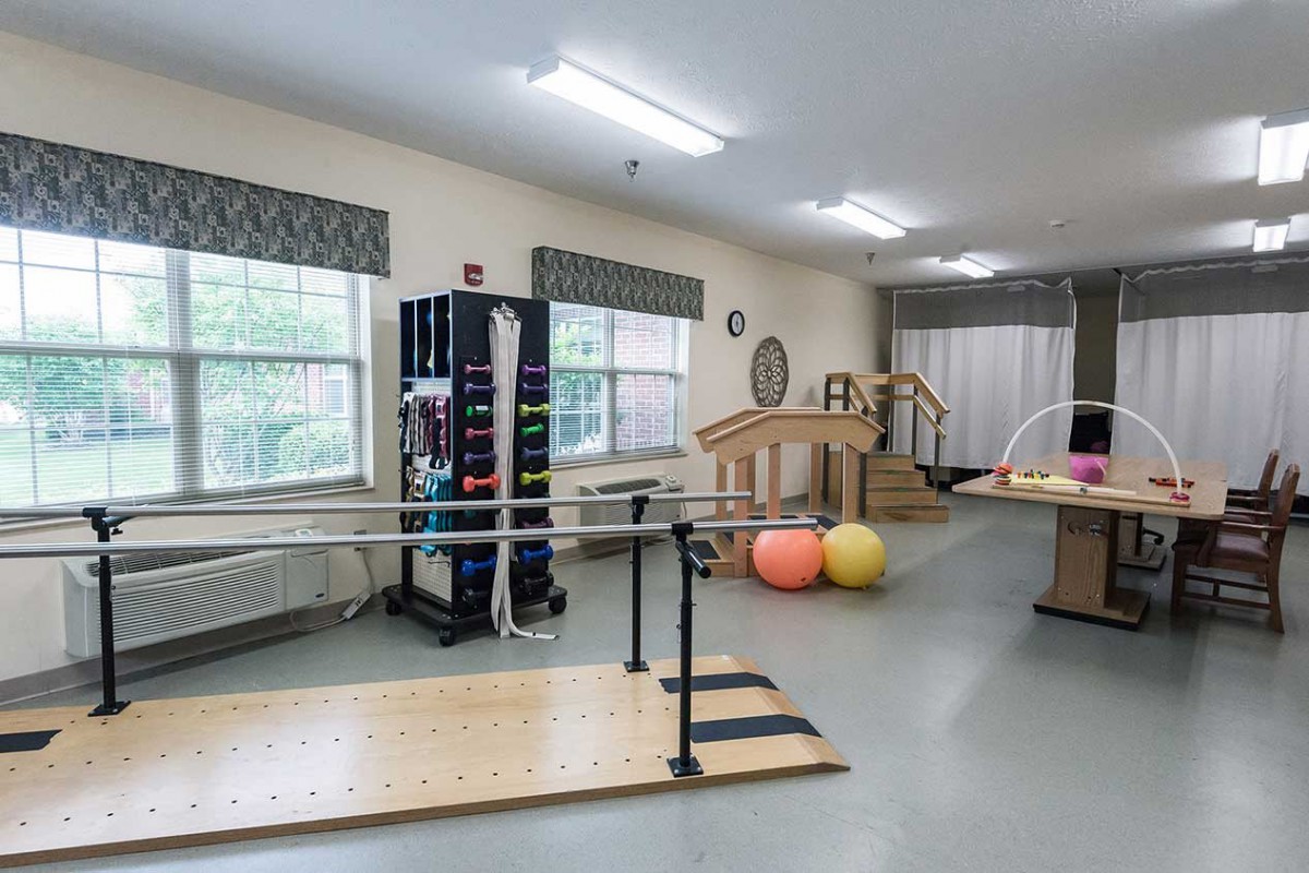 A well-equipped physical therapy room with exercise equipment and parallel bars.