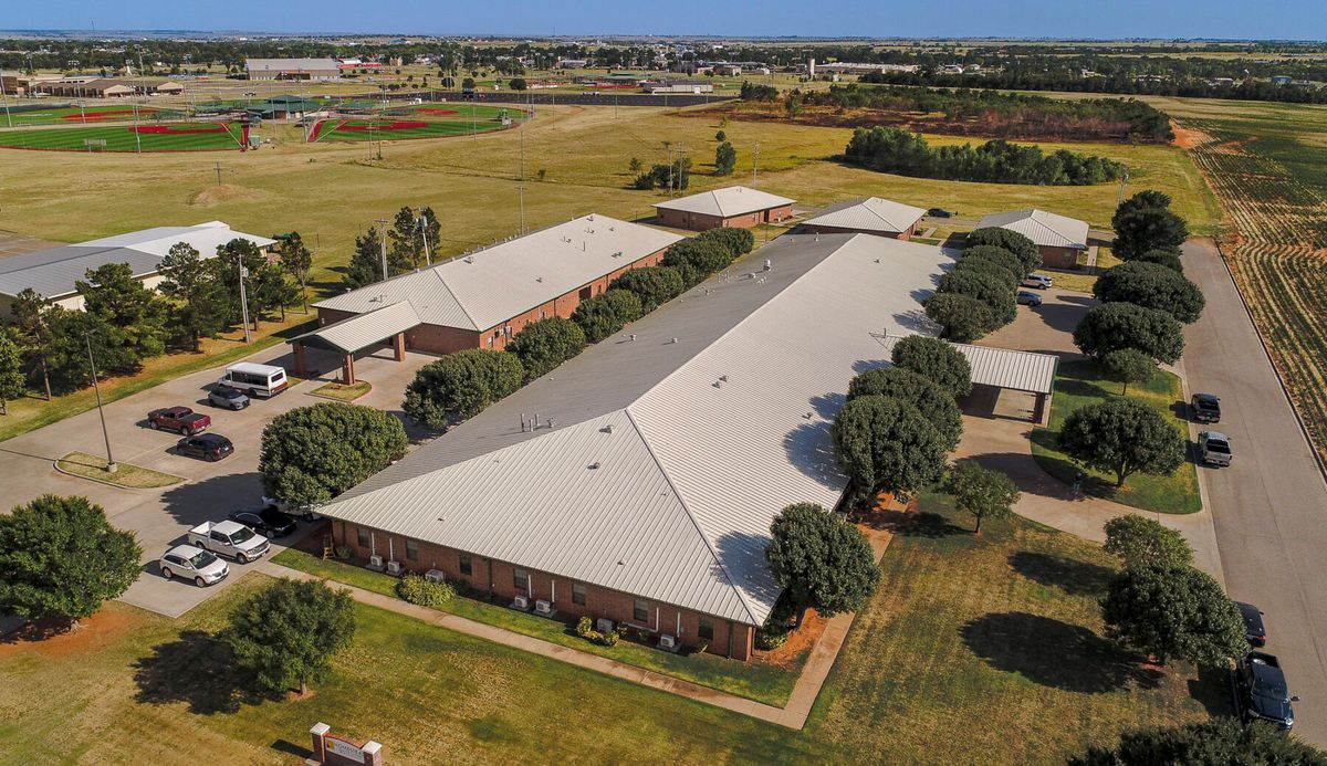 Aerial view of a large building with a white roof surrounded by trees and fields in the countryside.