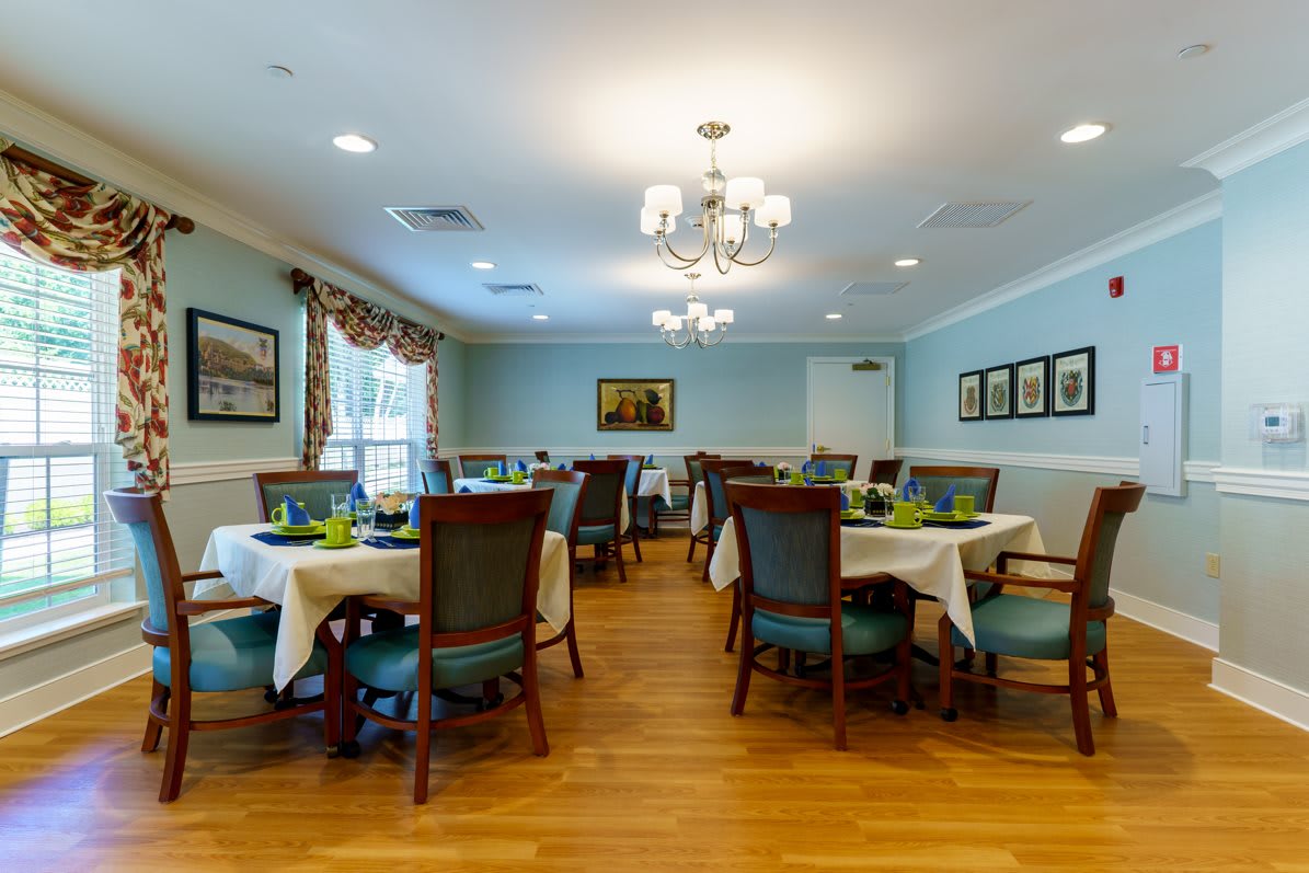 A spacious dining room with neatly arranged tables and chairs, featuring elegant chandeliers and a polished wooden floor.