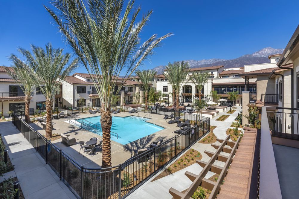 A modern apartment complex with a central swimming pool, surrounded by palm trees and outdoor seating areas.